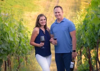 man and women holding glass of wine standing in the vineyard